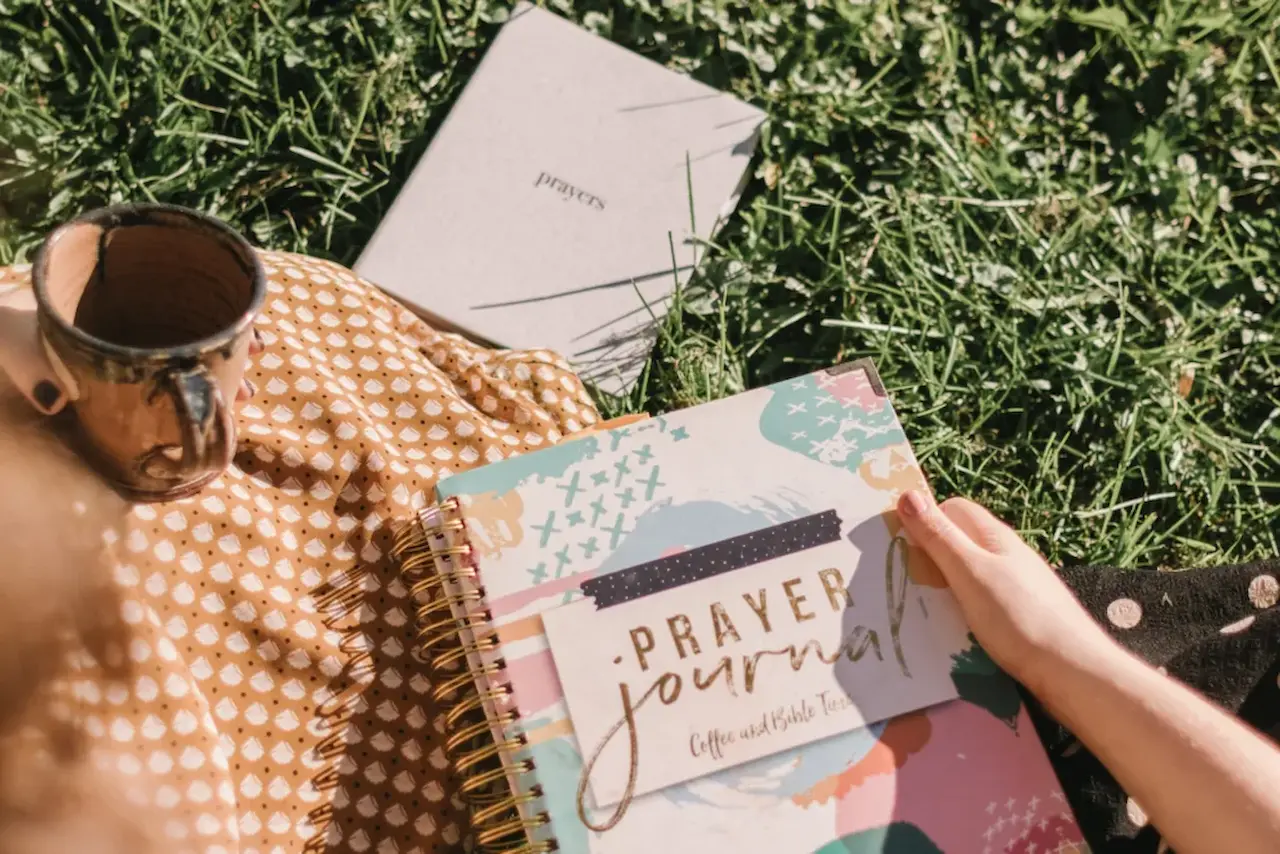 Christian writing in a prayer journal with an open Bible, reflecting on prayers, gratitude, Scripture, and spiritual growth through faith.
